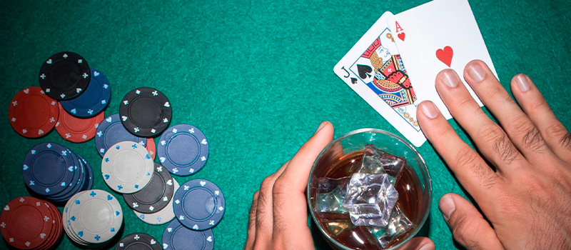 Manos de jugador sobre mesa de casino con cartas y bebida